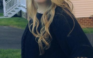 A young woman smiling in front of a house.