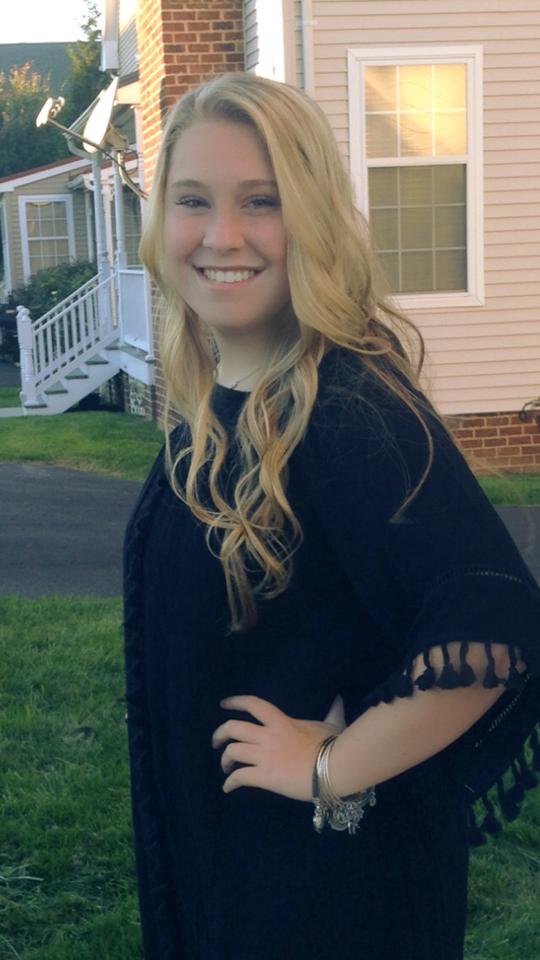 A young woman smiling in front of a house.