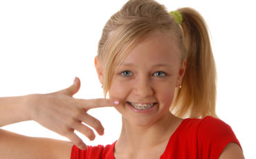 A young girl with braces pointing to her finger.