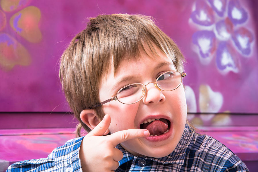 A young boy with glasses and a finger in his mouth.