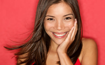 A smiling asian woman posing on a red background.