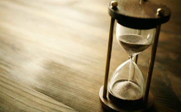 A sand hourglass sitting on a wooden table.