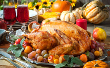 A thanksgiving turkey on a platter with grapes and wine glasses.