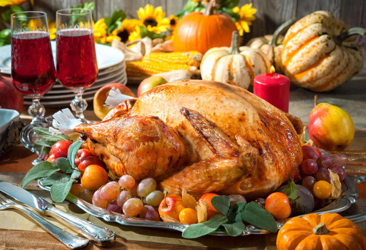 A thanksgiving turkey on a platter with grapes and wine glasses.