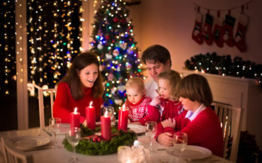 A family sits at a christmas dinner table with candles.