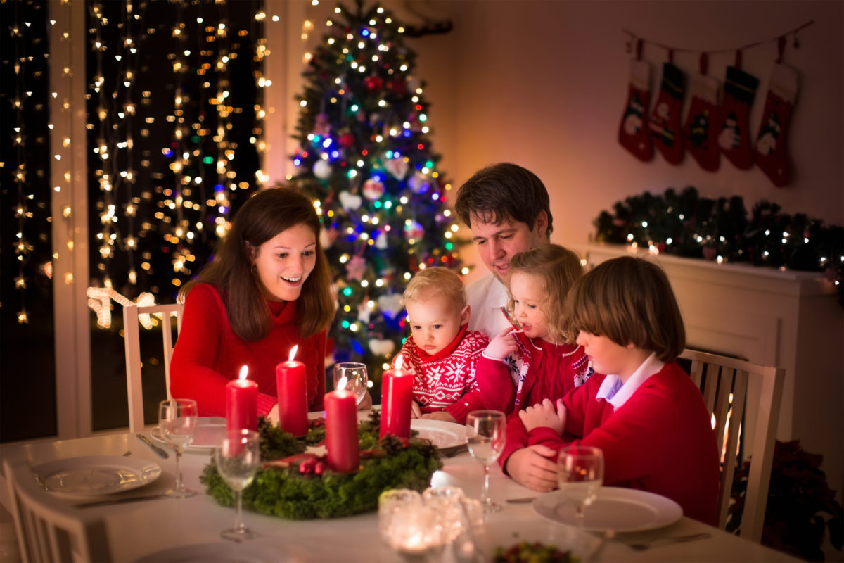 A family sits at a christmas dinner table with candles.