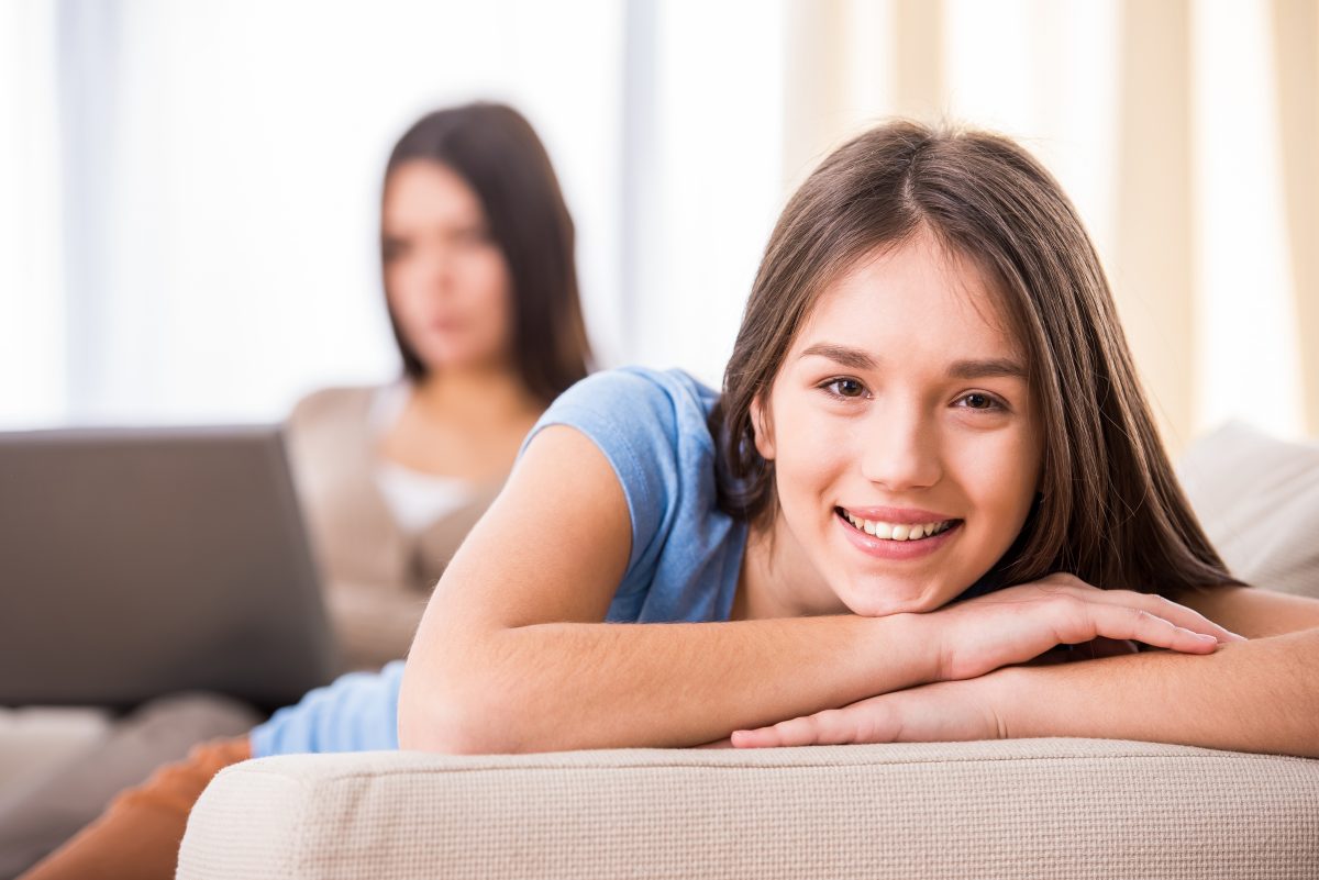 A young girl is laying on a couch with her mother.