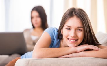 A young girl is laying on a couch with her mother.