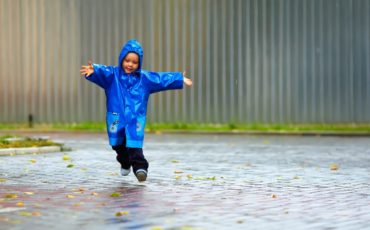A child in a blue raincoat is running in the rain.