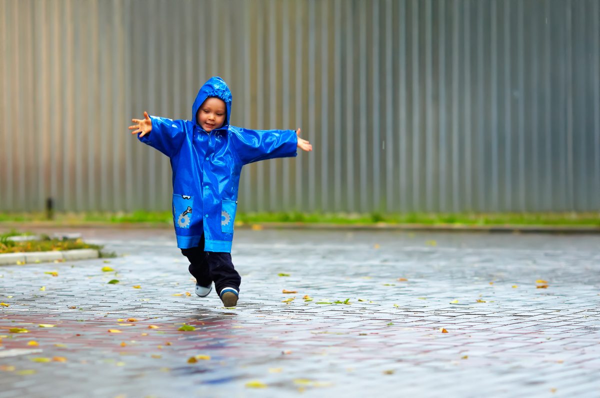 A child in a blue raincoat is running in the rain.