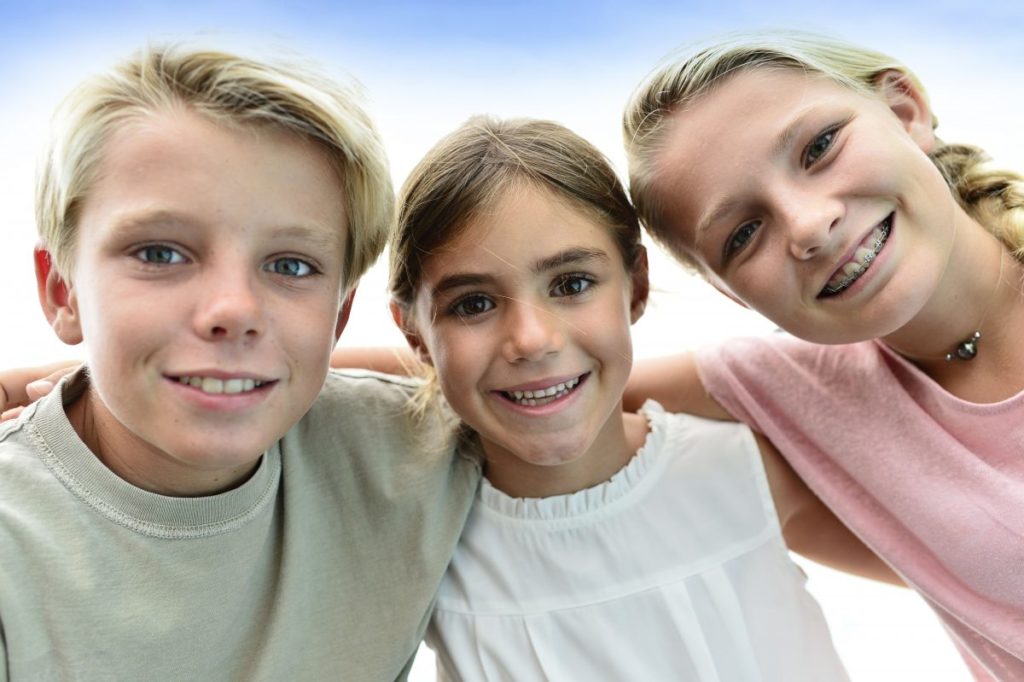 Three children posing for a photo in front of a blue sky.