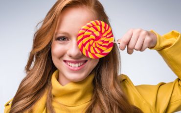 A girl is holding a lollipop in front of her face.