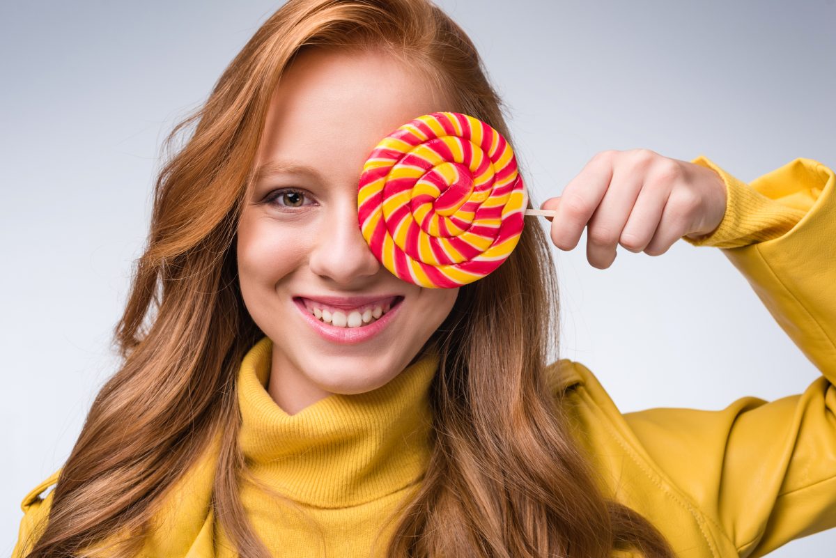 A girl is holding a lollipop in front of her face.