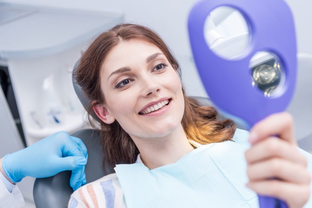 A woman in a dentist's chair holding a magnifying glass.