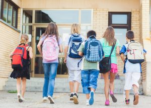 A group of children with backpacks walking out of a building.