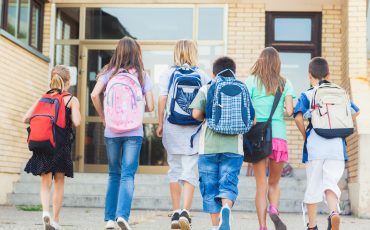 A group of children with backpacks walking out of a building.