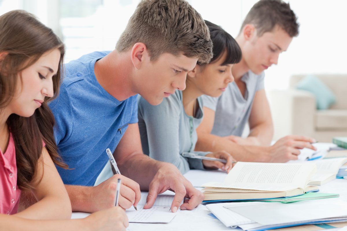 A group of people sitting at a table and writing.