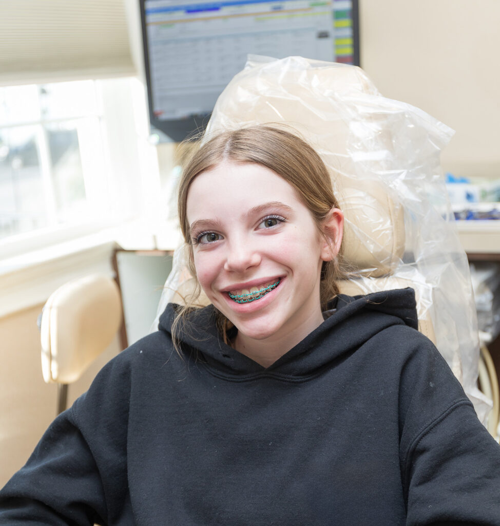 Teenage patient, sitting in an exam chair, smiling with braces.